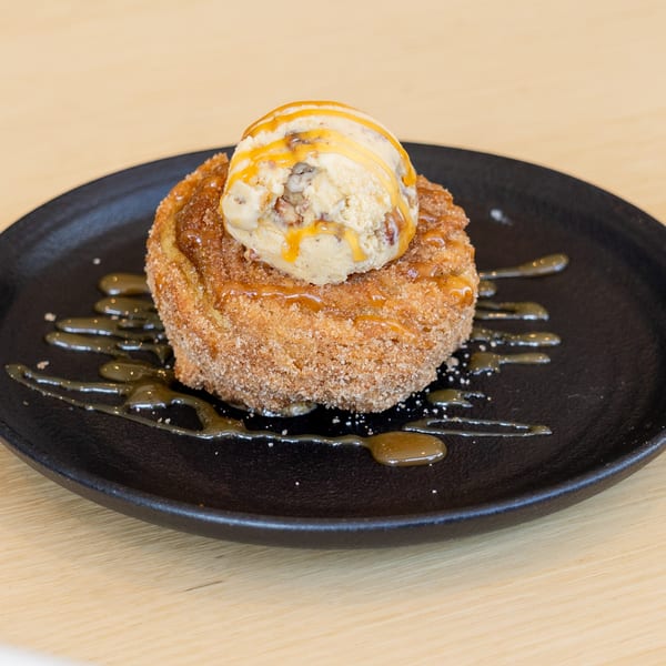 Churro dessert with a scoop of ice cream and caramel drizzle on a black plate.