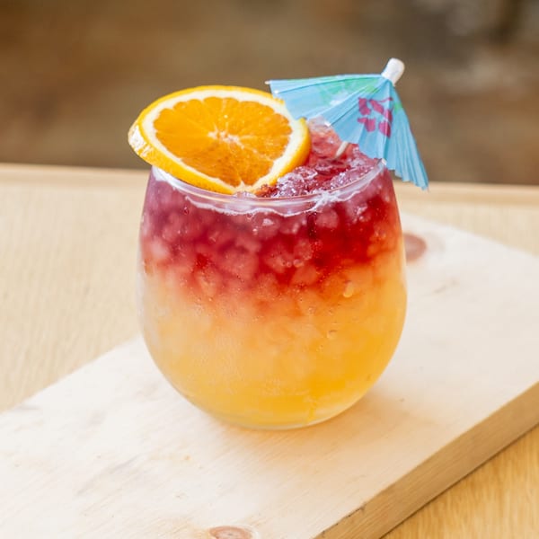 El Barrio's vibrant, layered cocktail with crushed ice, an orange slice, and a blue umbrella.
