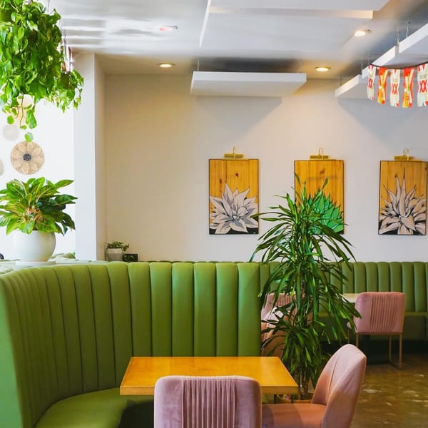 El Barrio Cantina interior with green booths, pink chairs, wooden tables, and agave artwork.