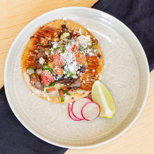 El Barrio's carne asada taco with pico de gallo, cheese, lime, and radishes on a plate.
