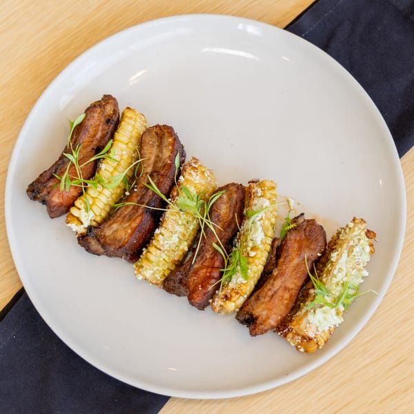 Grilled Mexican street corn and ribs on a white plate, garnished with fresh herbs.