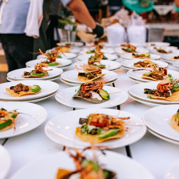 Numerous plates of El Barrio Mexican appetizers, featuring shrimp, avocado, and tortillas, arranged on a white table.