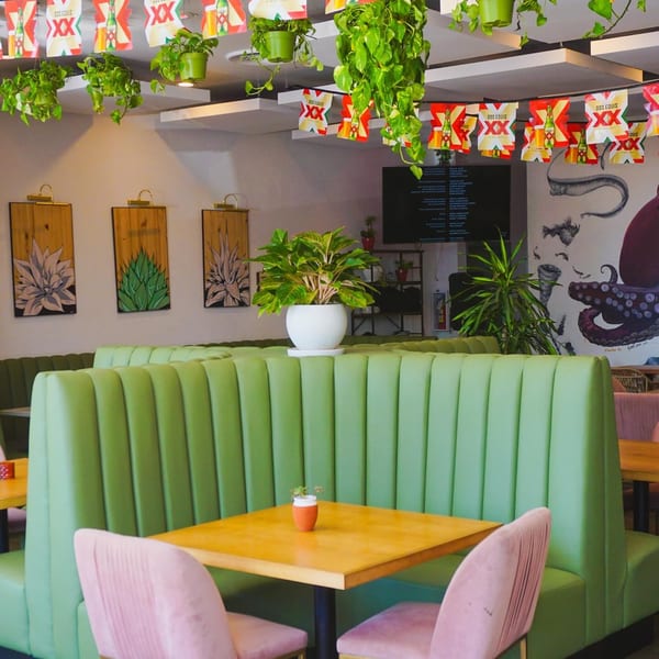 El Barrio's vibrant dining area with green booths, wooden tables, pink chairs, and agave artwork.