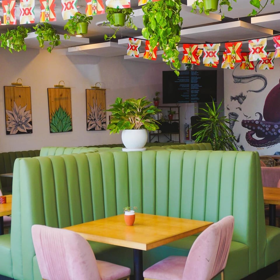 El Barrio's vibrant dining area with green booths, wooden tables, pink chairs, and agave artwork.