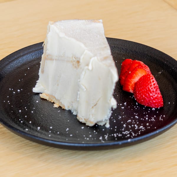 Slice of El Barrio's tres leches cake with strawberries on a black plate.