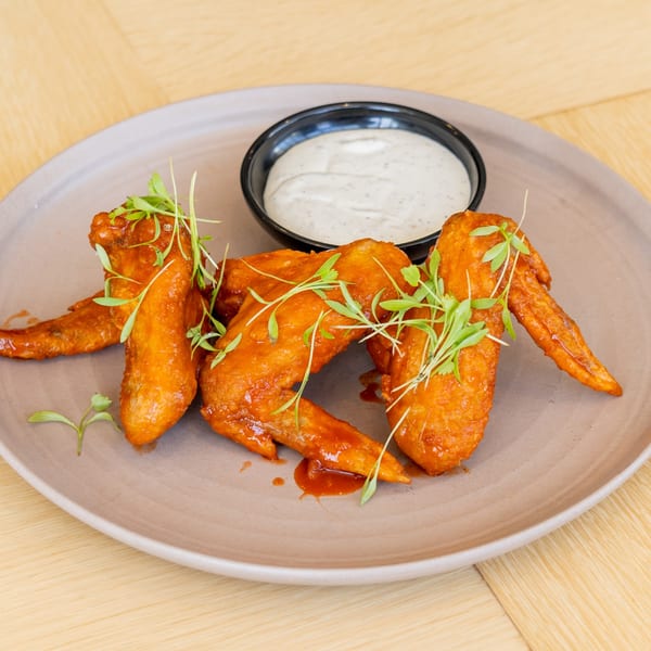 Four El Barrio chicken wings, glazed in orange sauce and garnished with microgreens, served with a side of ranch.