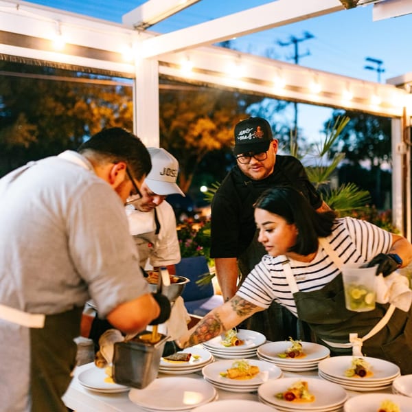 El Barrio chefs plating Mexican dishes on a brightly lit outdoor patio at dusk.