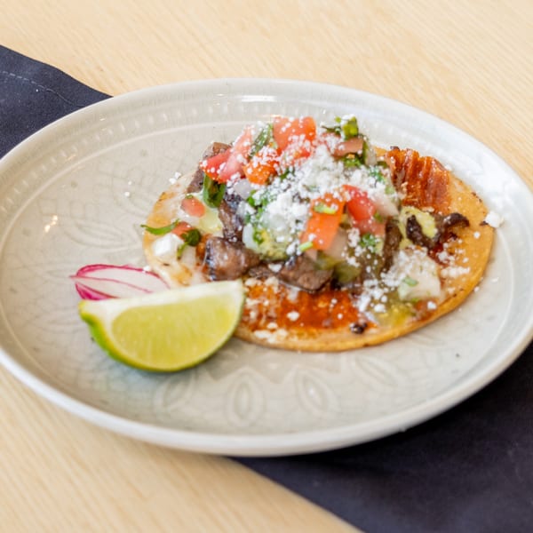 El Barrio's Mexican tostada with meat, pico de gallo, cheese, and a lime wedge.