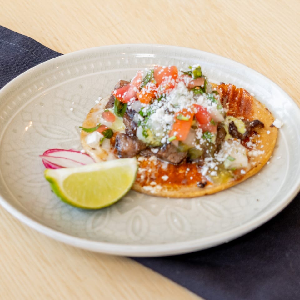El Barrio's Mexican tostada with meat, pico de gallo, cheese, and a lime wedge.