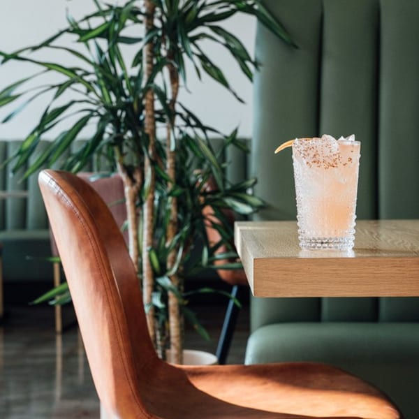 A pink El Barrio cocktail with a chili-salt rim and grapefruit garnish sits on a wooden table.